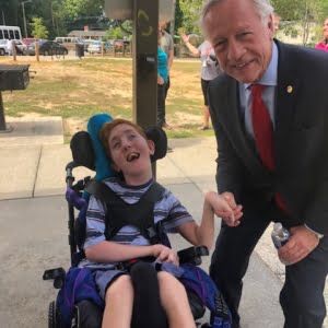 Young man in a wheelchair beside a grey headed man smiling at camera